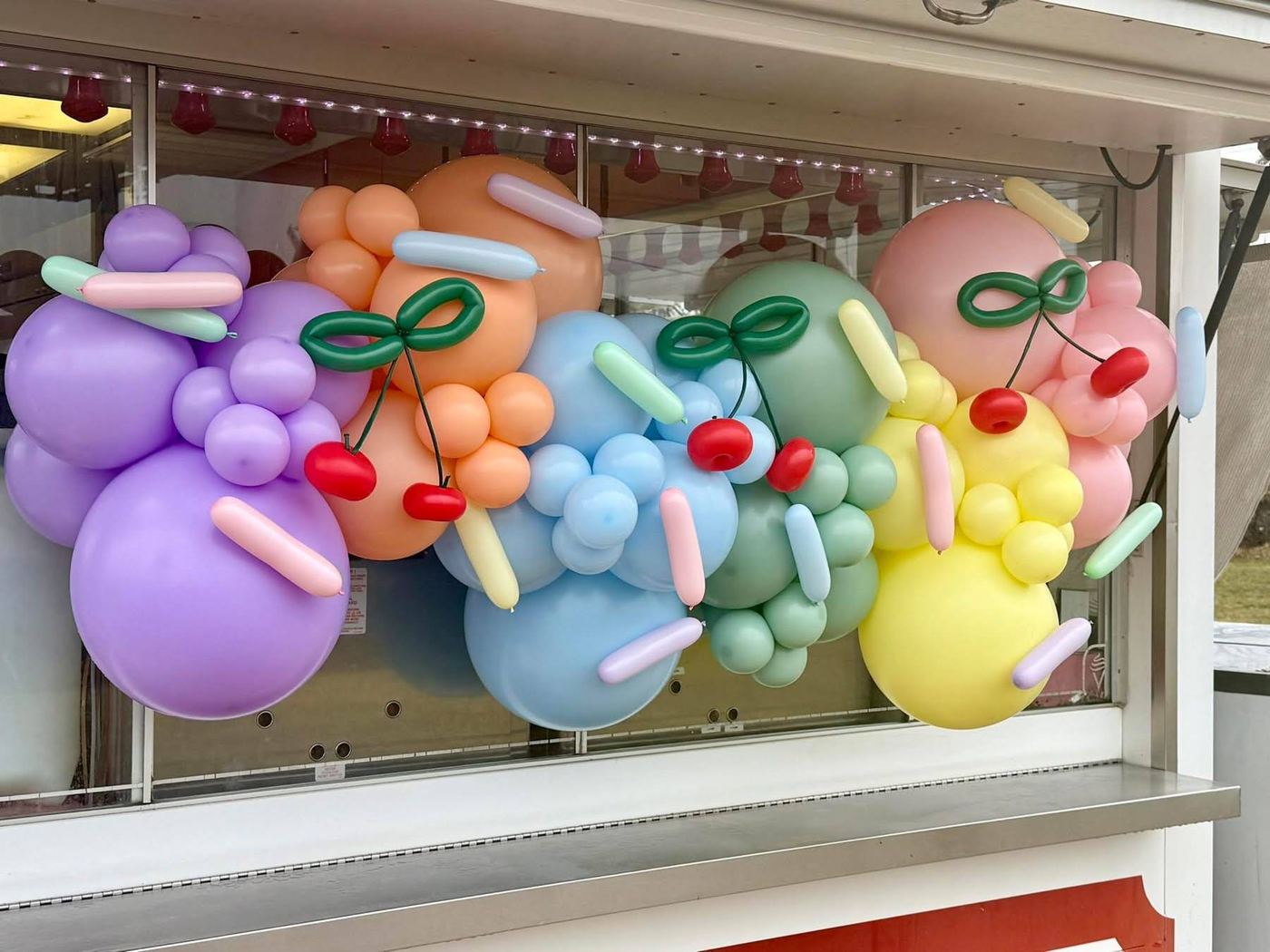 Pastel balloon garland with cherry and sprinkle balloon details across a window