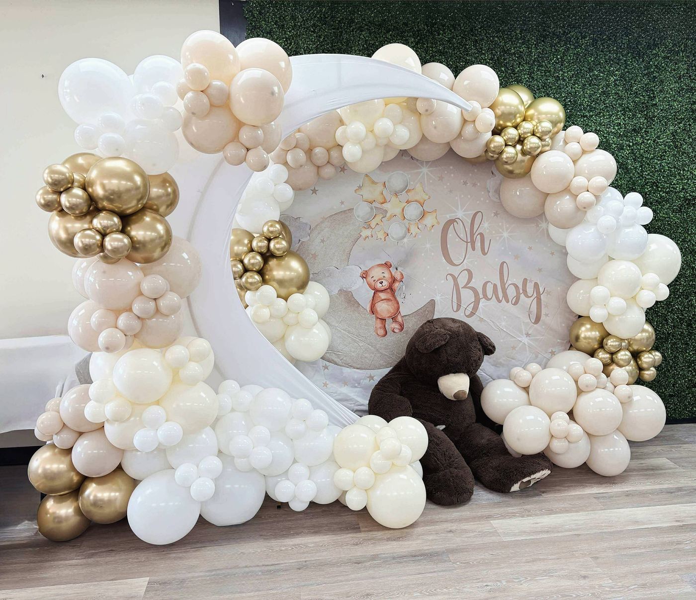 White, cream and gold balloon garland around a round Oh Baby backdrop with a plush bear