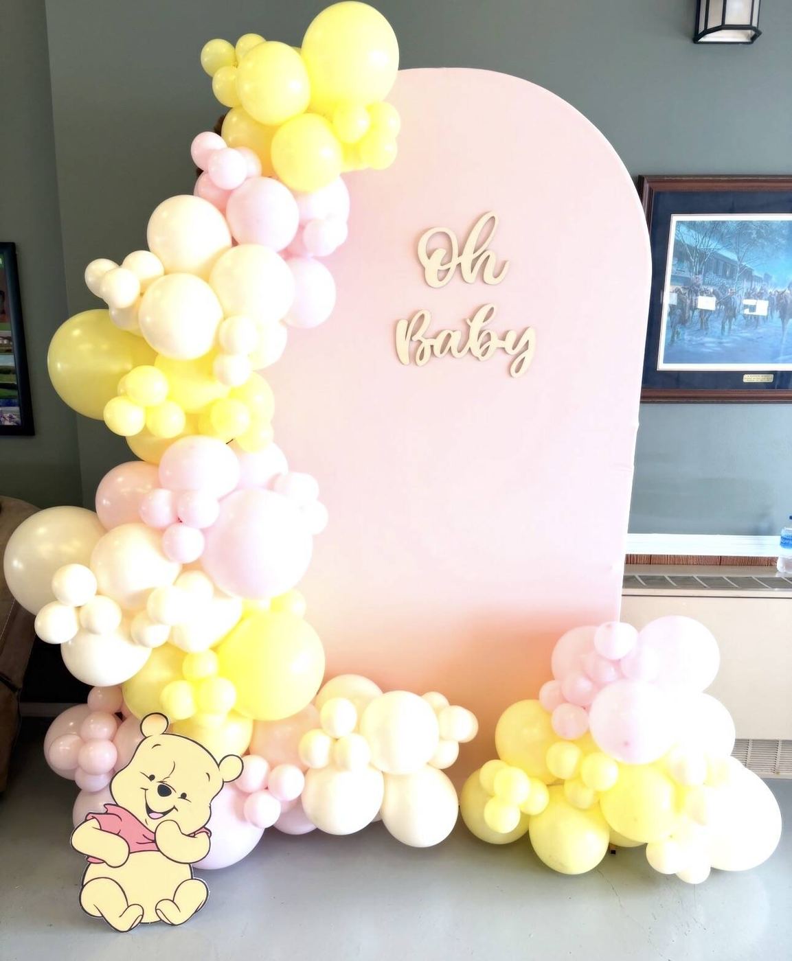 Pastel yellow, pink and white garland on an Oh Baby arch with a Winnie the Pooh figure