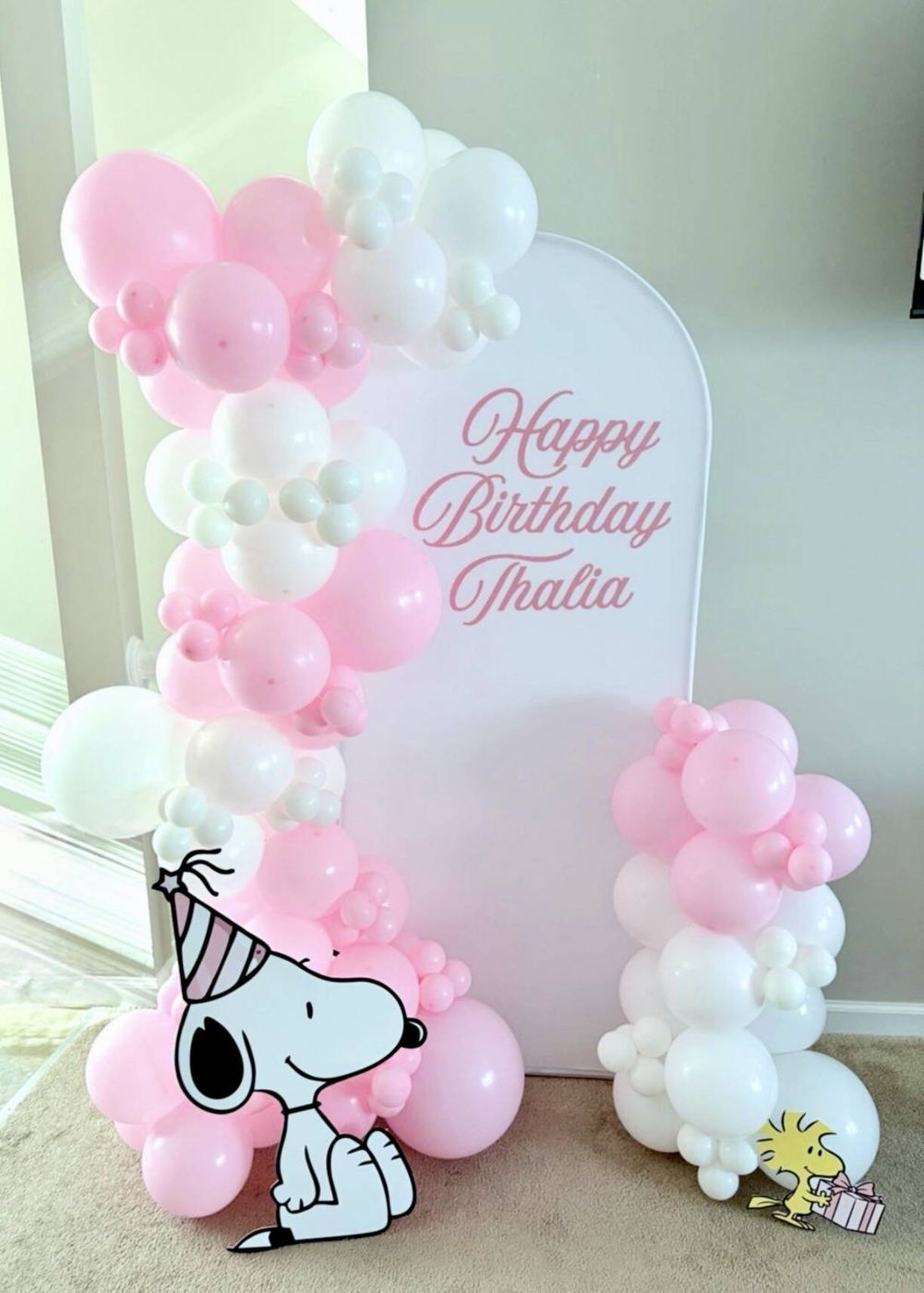 Pink and white balloon garland on a personalized Happy Birthday arch with a Snoopy cutout