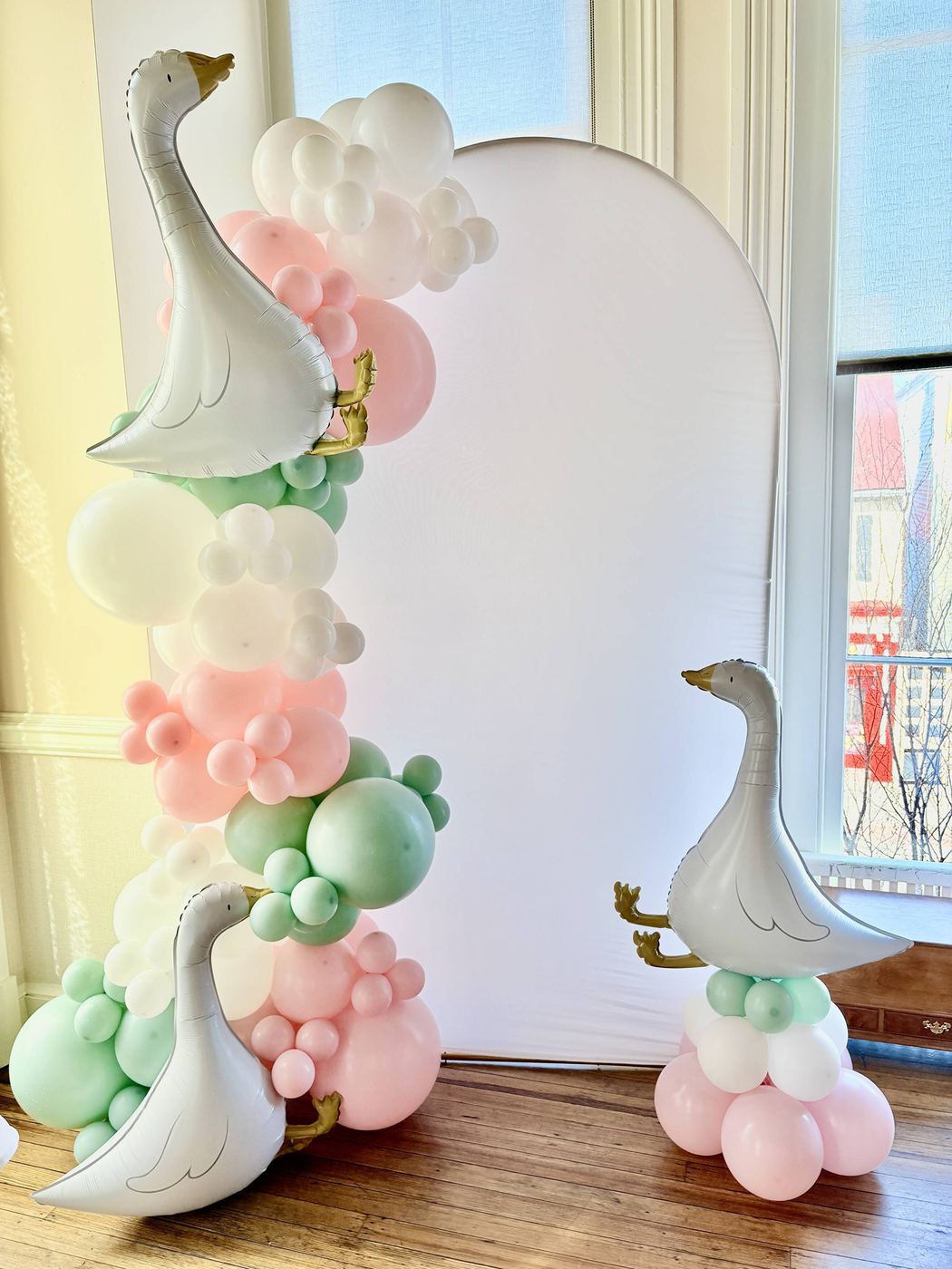 Pastel balloon garland with white stork balloons beside an arched backdrop
